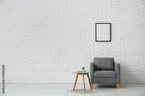 Armchair, coffee table with magazine and houseplant near white brick wall in room