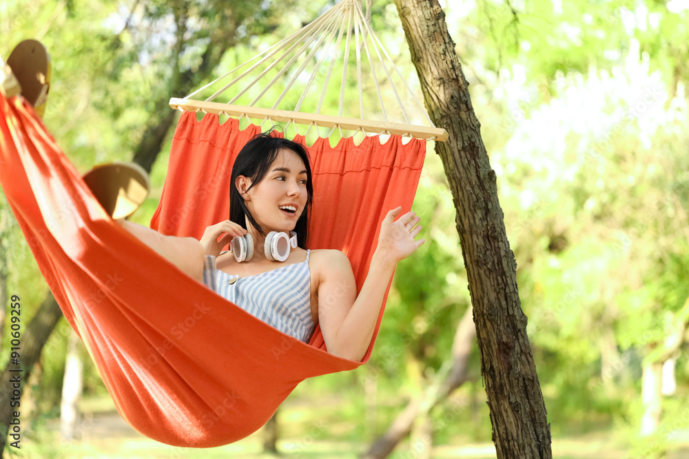Naklejka premium Young woman with headphones relaxing in hammock outdoors