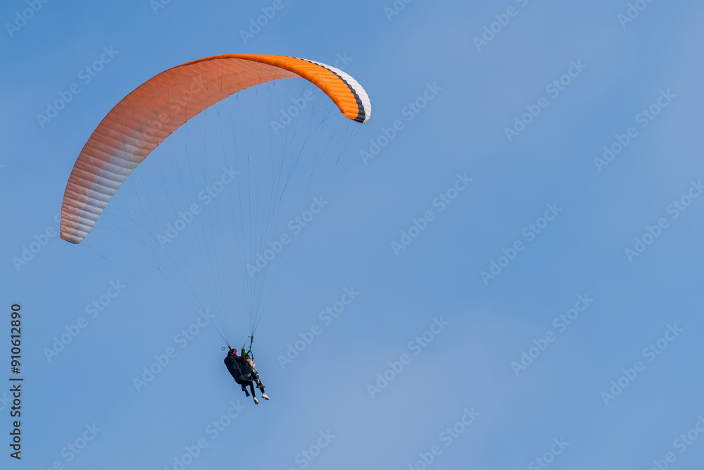 An orange-and-white paraglider flying in the sky An orange-and-white paraglider flying in the sky