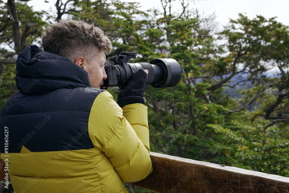 Male photographer in winter jacket captures images with a telephoto lens amidst forest trees. Male photographer in winter jacket captures images with a telephoto lens amidst forest trees.
