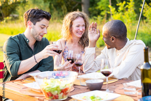 Three friends are enjoying each others company outdoors, sharing wine and food while creating joyful memories together