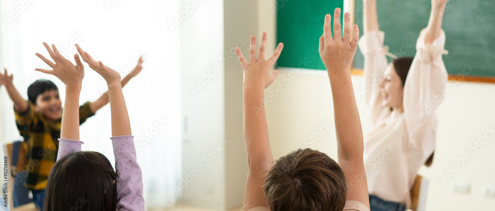 Enthusiastic children with hands raised in a diverse classroom ...