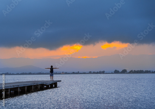 Young man with open arms on the pier of the Trabucador beach in the Ebro Delta at sunset. photo