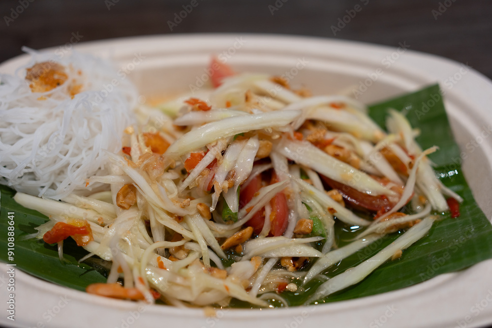 Thai spicy green papaya salad served with rice vermicelli on banana leaf and paper dish. Close up Thai spicy green papaya salad served with rice vermicelli on banana leaf and paper dish. Close up