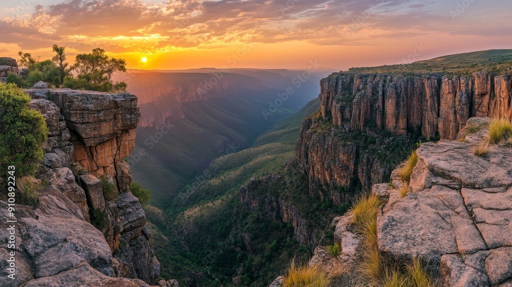 Fototapeta premium Panoramic View of Rugged Mountain Landscape at Sunset, Dramatic Cliffs and Deep Gorges with Sky Ablaze in Warm Hues of Orange and Pink