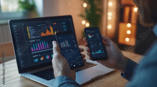 close-up A businessman is seated at his desk with a laptop, examining financial report presentation, utilizing a smartphone, and holding a phone with graphs and diagrams displayed.