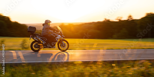 Driver riding motorcycle on empty road during sunset photo