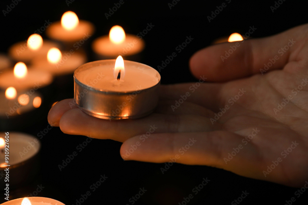 Woman holding burning tealight candle on black background, closeup Woman holding burning tealight candle on black background, closeup