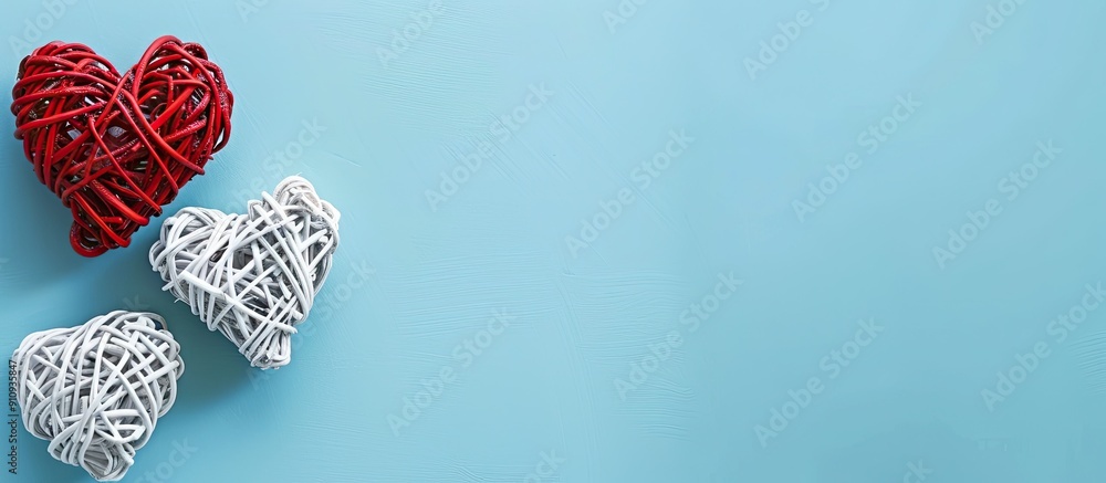 Fototapeta premium Valentine s Day themed flat lay featuring white rattan hearts with a red heart on a blue background ideal for a greeting card with copy space image