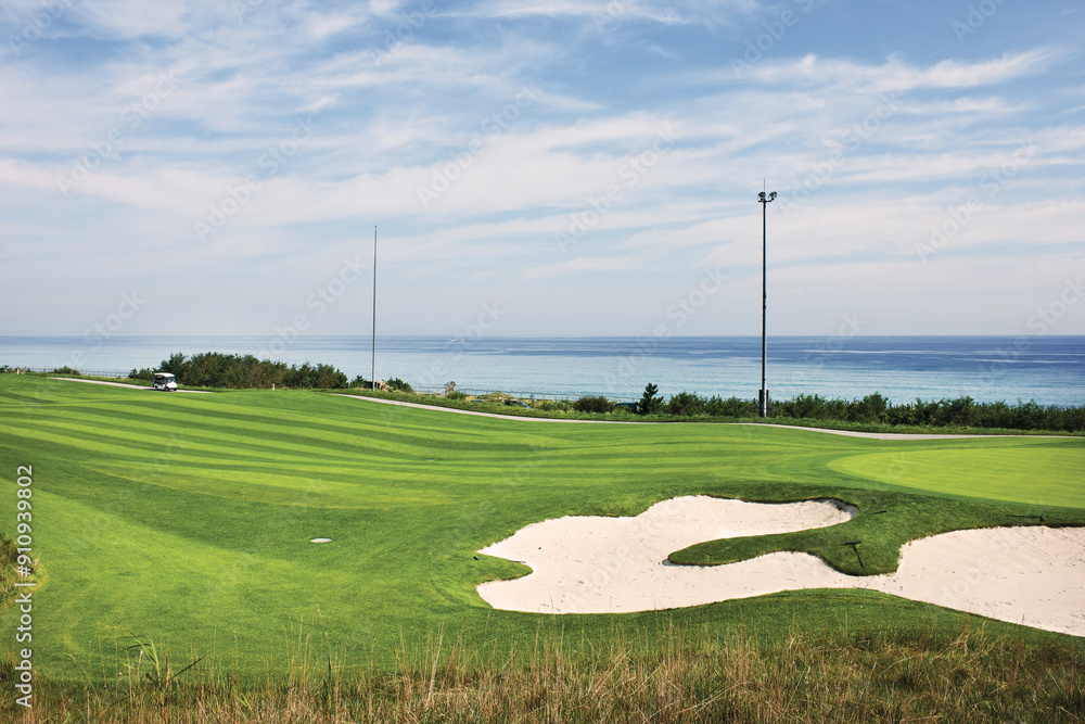 Obraz premium 푸른하늘에 녹색잔디가 있고 바다가 보이는 골프장풍경.