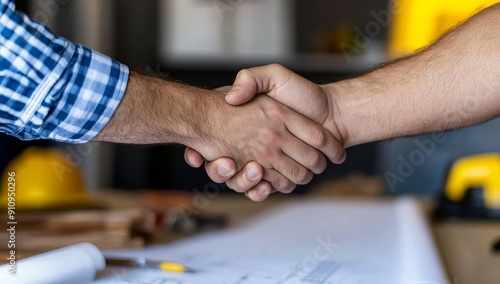 Two construction workers shaking hands over table with blueprints and tools