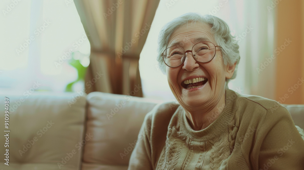 An elderly woman with glasses beams joyfully while sitting on a couch in a sunlit living room, conveying warmth and happiness. An elderly woman with glasses beams joyfully while sitting on a couch in a sunlit living room, conveying warmth and happiness.