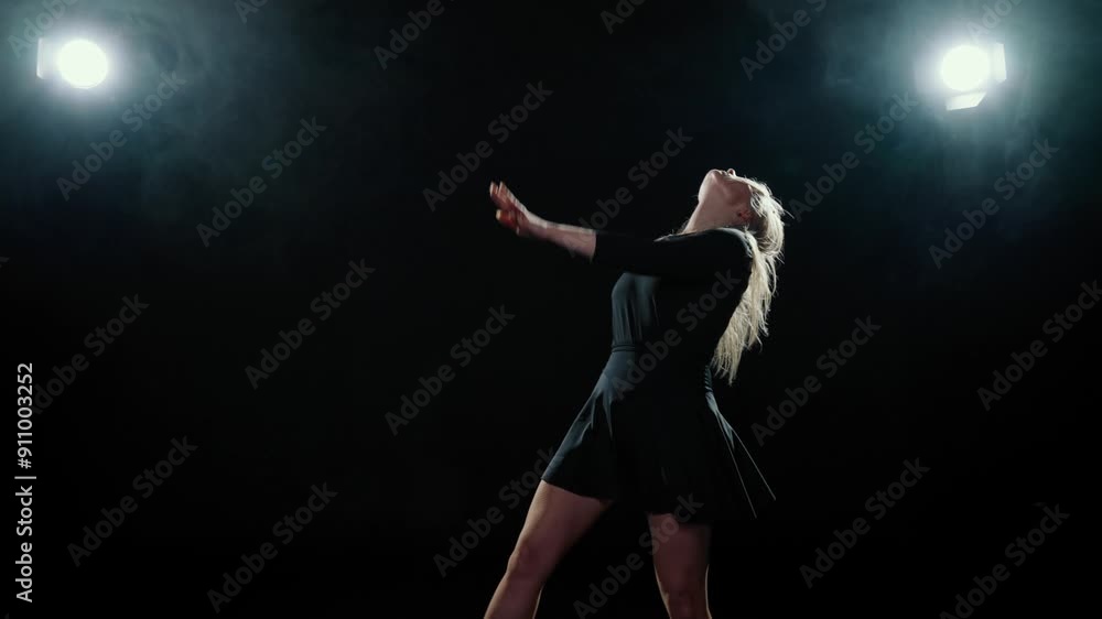Emotional blonde woman dancing alone in darkness, female figure in dark studio. Graceful female dancer performing contemporary choreography on stage with bright soffit, rehearsing dance movements Emotional blonde woman dancing alone in darkness, female figure in dark studio. Graceful female dancer performing contemporary choreography on stage with bright soffit, rehearsing dance movements