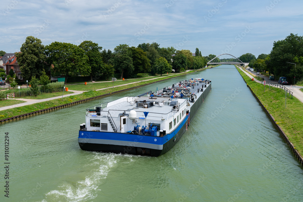 A barge moves smoothly through a tranquil canal lined with trees under a clear blue sky. A barge moves smoothly through a tranquil canal lined with trees under a clear blue sky.