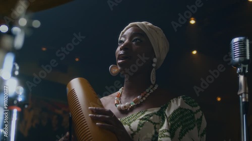 Black young woman playing guiro and singing in music studio while getting ready for performance photo