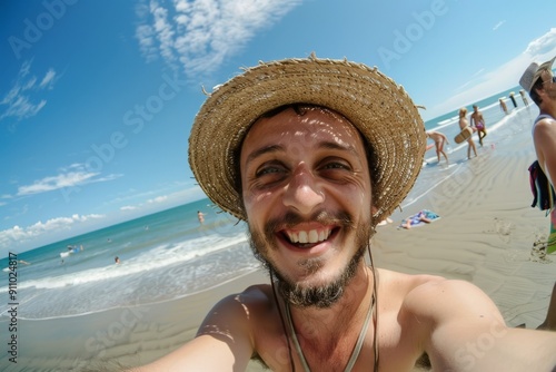 A beaming man in a straw hat takes a selfie at the beach on a sunny day, radiating joy and showcasing the lively, carefree atmosphere amidst the backdrop of sea and sand.