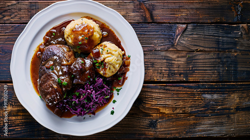 Delicious meal with red cabbage, dumplings and meat with gravy served on a white plate, resting on a rustic wooden table photo