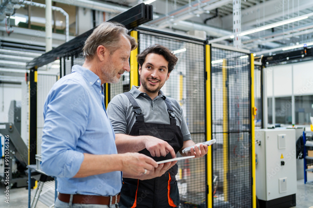 Smiling colleague holding machine part and discussing with manager standing on production floor Smiling colleague holding machine part and discussing with manager standing on production floor
