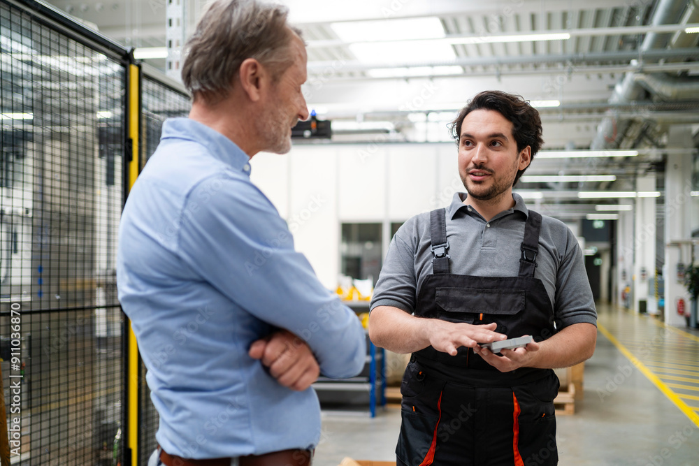 Colleague in apron explaining machine part to manager in factory Colleague in apron explaining machine part to manager in factory
