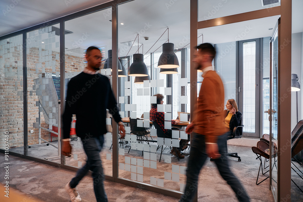In the dynamic hustle and bustle of a business environment, a group of young business professionals walk down the corridor next to their office, while their colleagues collaborate inside, symbolizing In the dynamic hustle and bustle of a business environment, a group of young business professionals walk down the corridor next to their office, while their colleagues collaborate inside, symbolizing