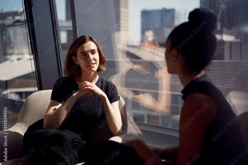 Young businesswoman discussing with colleague sitting near window at office Young businesswoman discussing with colleague sitting near window at office