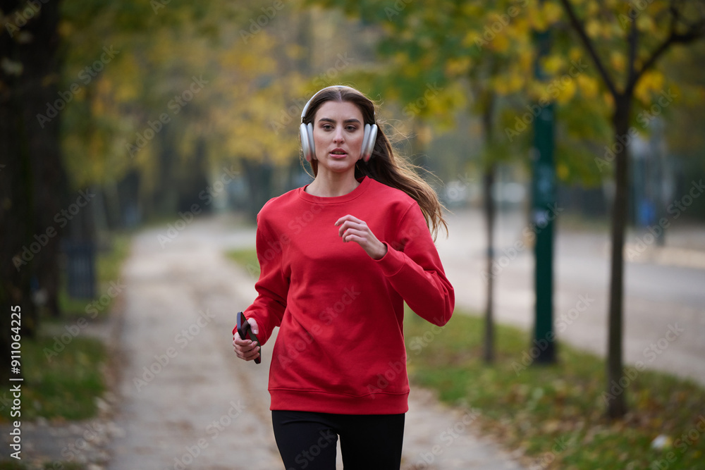 Young beautiful woman running in autumn park and listening to music with headphones on smartphone
