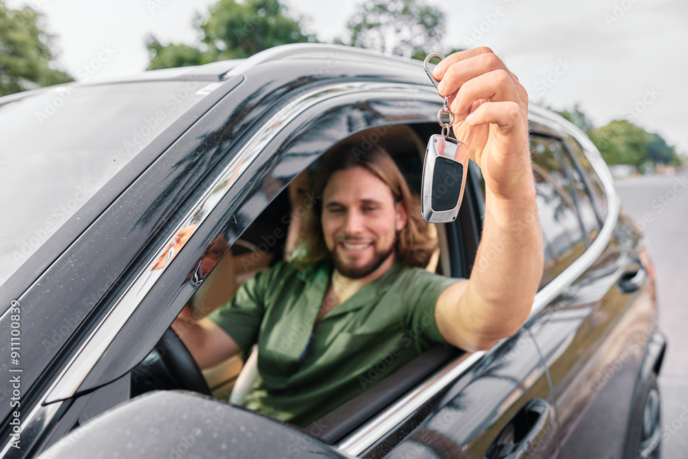 Naklejka premium Happy man showing car keys from a modern SUV while sitting in the driver s seat on a sunny day
