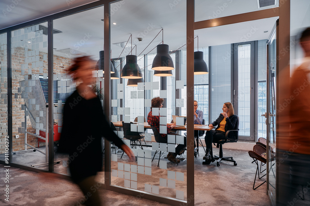 Fototapeta premium In the dynamic hustle and bustle of a business environment, a group of young business professionals walk down the corridor next to their office, while their colleagues collaborate inside, symbolizing