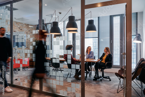 In the dynamic hustle and bustle of a business environment, a group of young business professionals walk down the corridor next to their office, while their colleagues collaborate inside, symbolizing photo