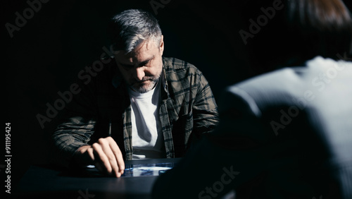 Detective showing photos of the crime scene to a male suspect in an interrogation room photo