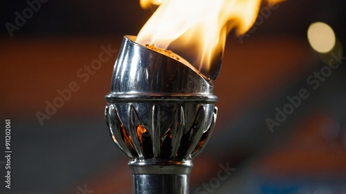 Silver torch with flame, stadium in background, concept of competition, sport and games.