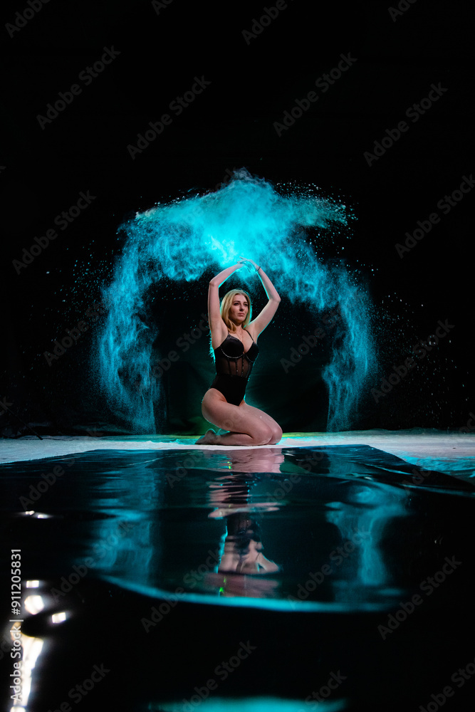 Young slim woman posing with blue particles sprayed in the air