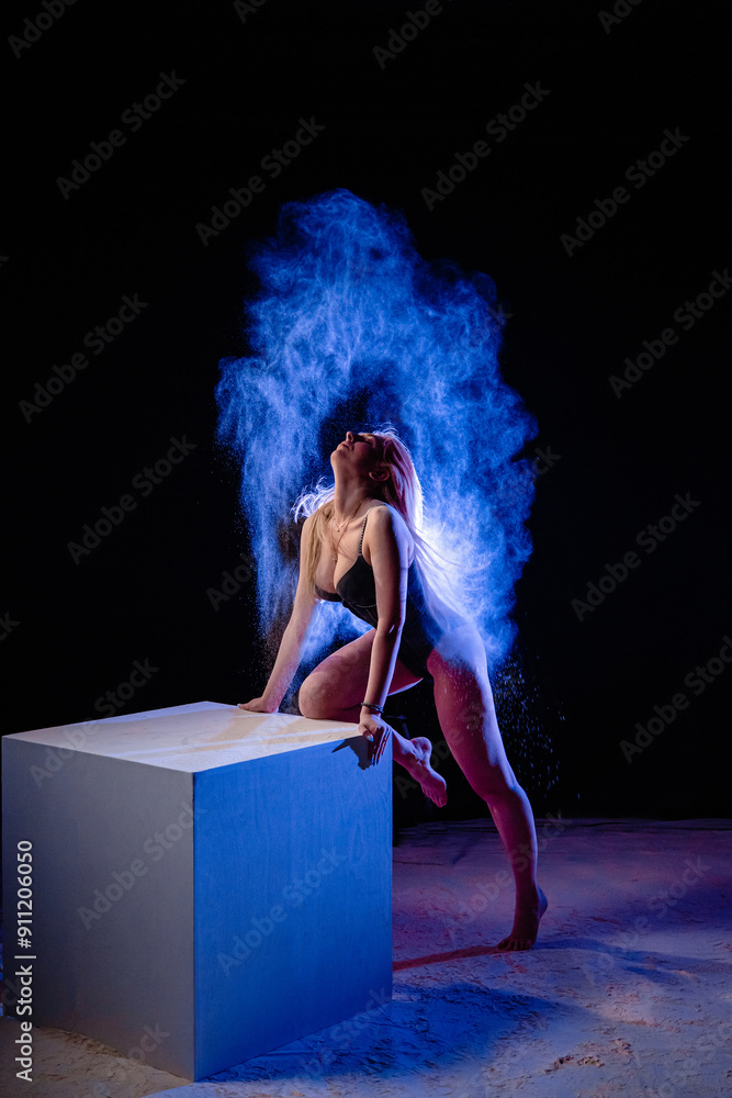 Young slim woman posing near the big white cube with spread a blue particles in the air