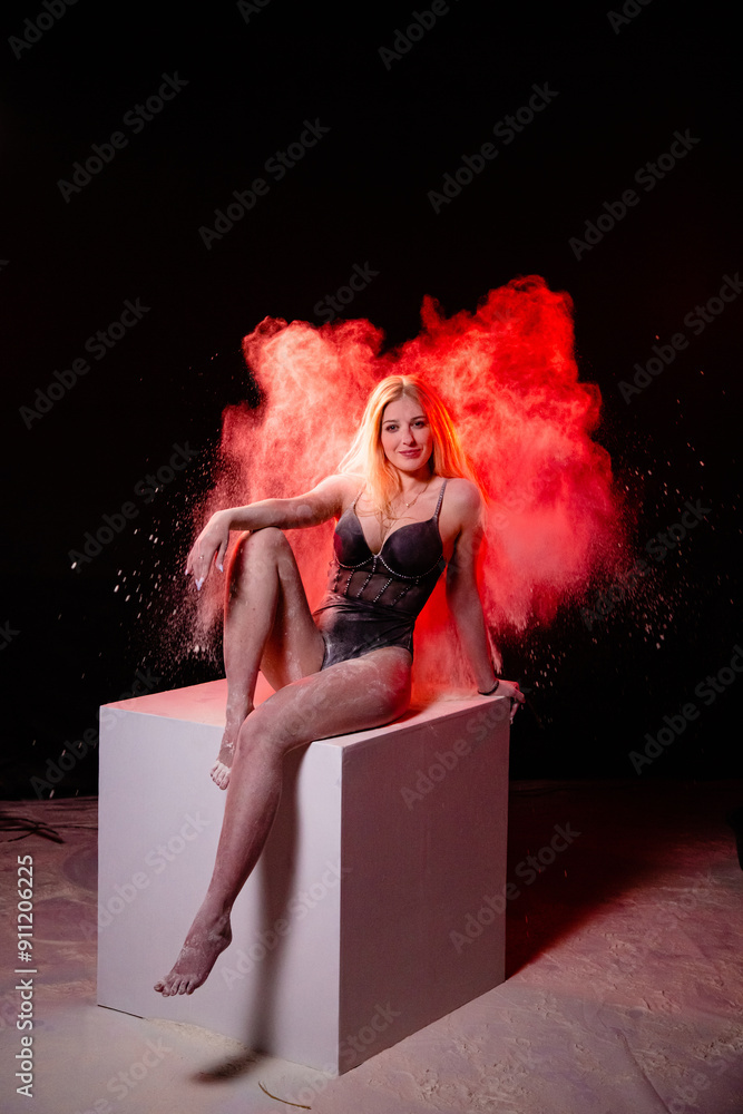 Young slim woman posing near the big white cube with spread red particles in the air