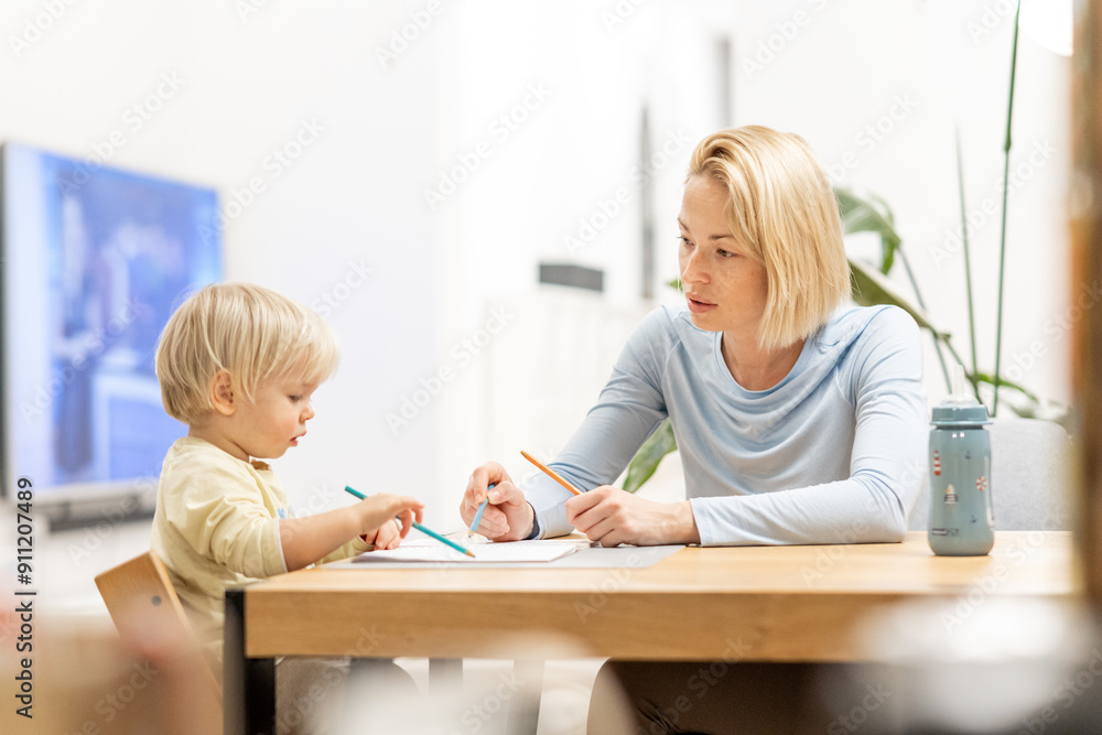 Caring young Caucasian mother and small son drawing painting in notebook at home together. Loving mom or nanny having fun learning and playing with her little 1,5 year old infant baby boy child Caring young Caucasian mother and small son drawing painting in notebook at home together. Loving mom or nanny having fun learning and playing with her little 1,5 year old infant baby boy child