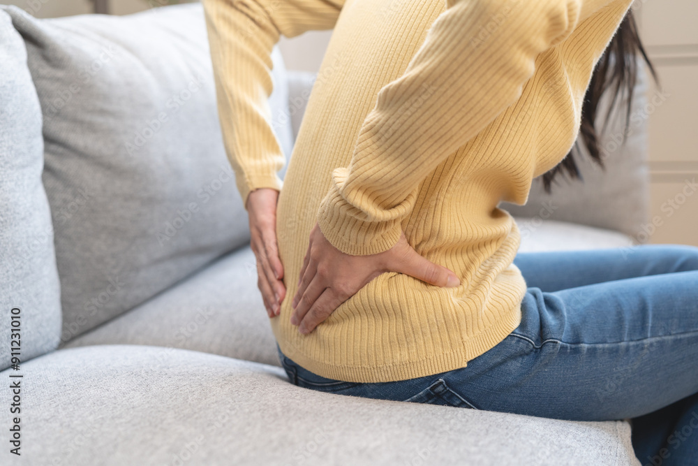 Close-up woman massaging her lower back has back pain because of sitting posture during work in office. Close-up woman massaging her lower back has back pain because of sitting posture during work in office.