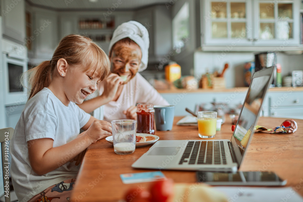 Happy mother and daughter having breakfast with monitor in kitchen Happy mother and daughter having breakfast with monitor in kitchen