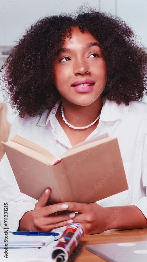Young positive dreamy African American woman reads book with romantic story about couple in love and imagines happy future and meeting handsome guy sits at table in kitchen. Literature, textbook Young positive dreamy African American woman reads book with romantic story about couple in love and imagines happy future and meeting handsome guy sits at table in kitchen. Literature, textbook