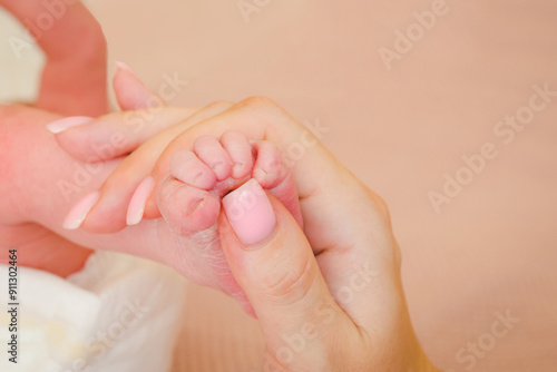 Small children's leg in mam's soft hands. Tenderness and love from birth. Care and raising of children health. Happy Family concept.