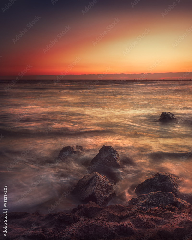 Obraz premium fascinating sunset over the sea reflecting on the sand and rocks