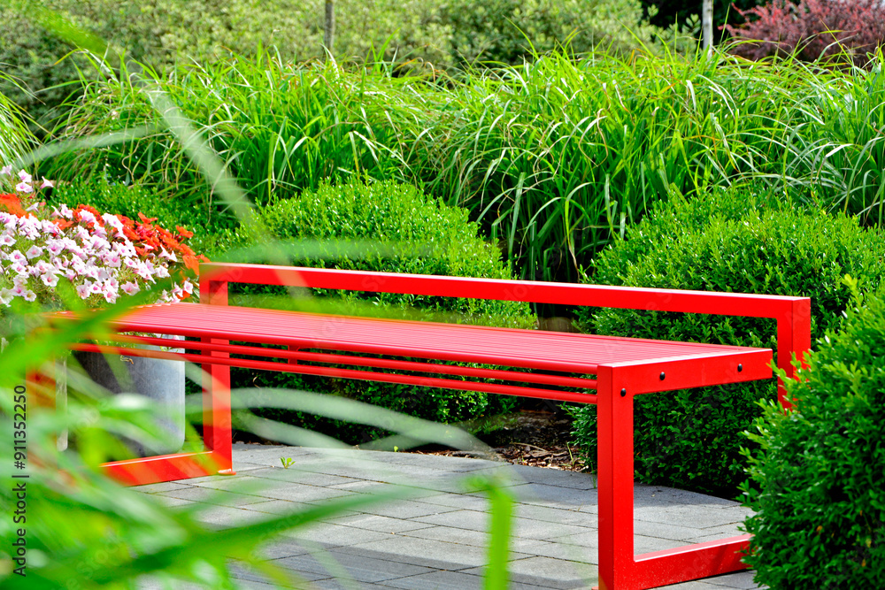 czerwona ławka ogrodowa z metalu na tle zilonych traw ozodbnych, metalowa ławka czerwona w ogrodzie, red metal garden bench and green ornamental grass, kącik wypoczynkowy, red metal bench in garden