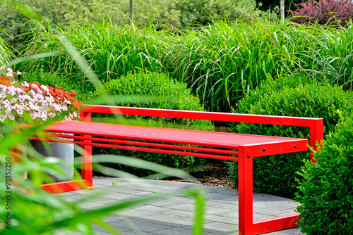 Obraz na płótnie czerwona ławka ogrodowa z metalu na tle zilonych traw ozodbnych, metalowa ławka czerwona w ogrodzie, red metal garden bench and green ornamental grass, kącik wypoczynkowy, red metal bench in garden w salonie