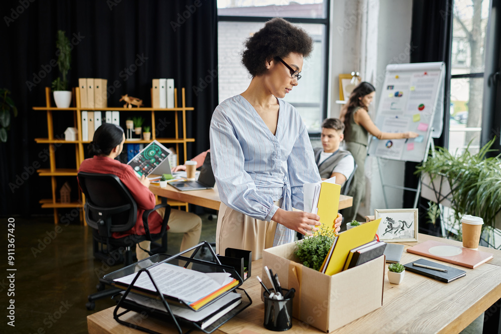 Trendy african american woman packing her items during lay off, colleagues on backdrop. Trendy african american woman packing her items during lay off, colleagues on backdrop.