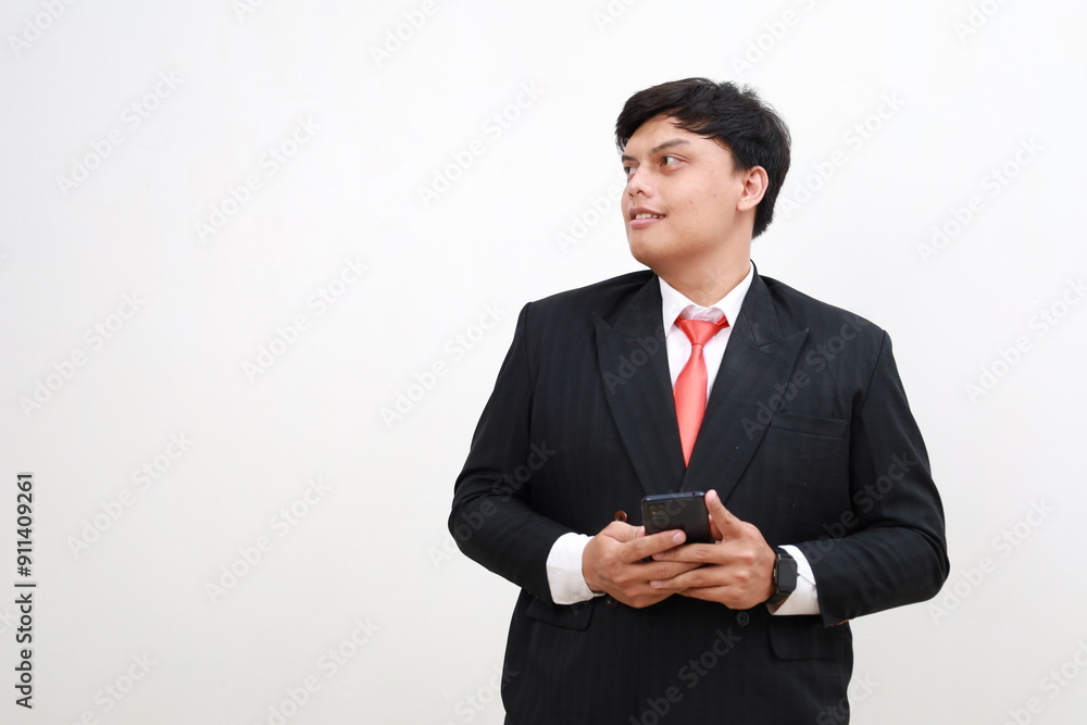 Smiling happy confident asian male company ceo executive wearing suit holding cellphone standing using business mobile apps technology financial online solutions on cell phone. Smiling happy confident asian male company ceo executive wearing suit holding cellphone standing using business mobile apps technology financial online solutions on cell phone.