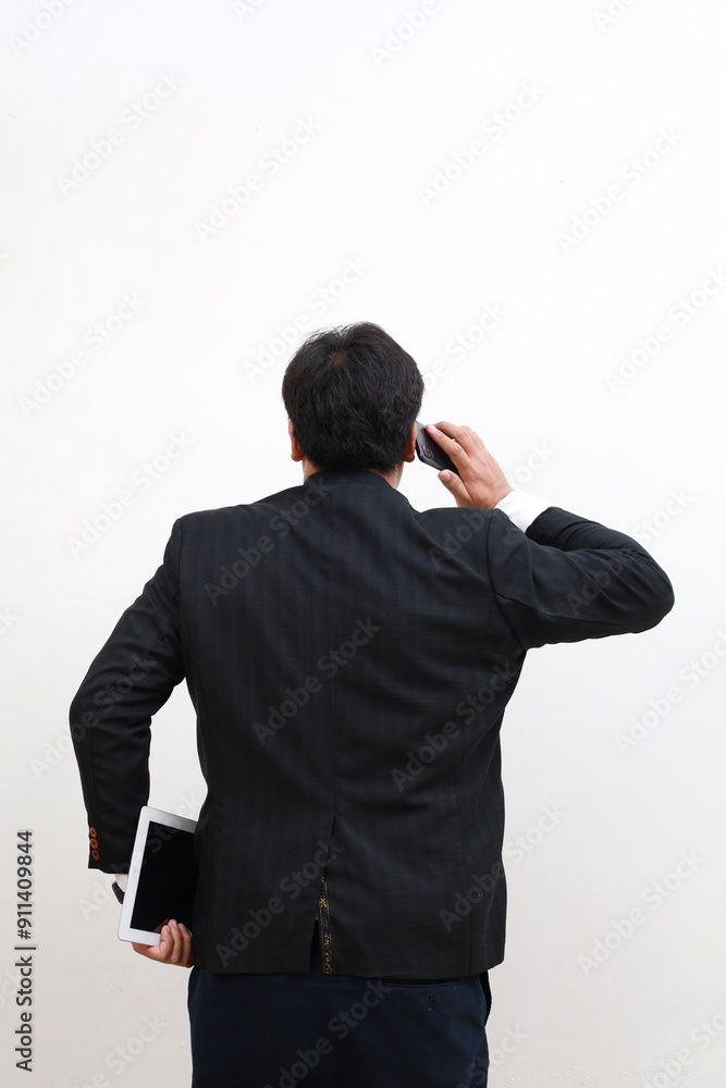 Back view portrait young businessman in blue suit holding tablet computer using smartphone. isolated on white background Back view portrait young businessman in blue suit holding tablet computer using smartphone. isolated on white background