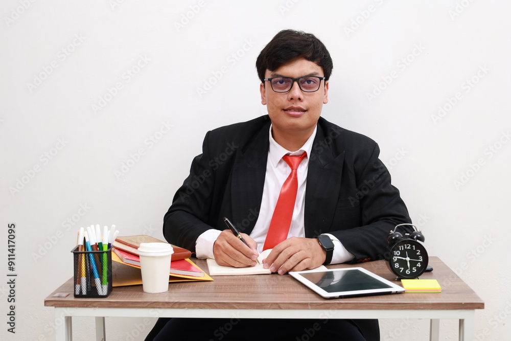 Smiling attractive young man working at a desk writing notes in a notebook conceptual of a hardworking office worker or businessman