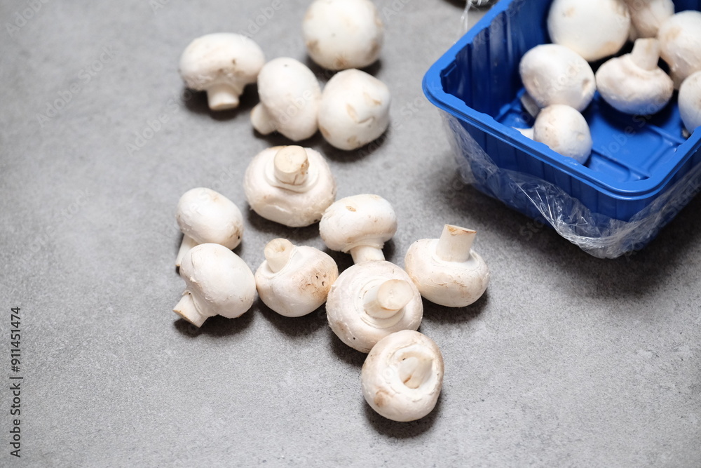 Raw mini mushroom champignon in a blue plastic box at gray background. Top view Raw mini mushroom champignon in a blue plastic box at gray background. Top view