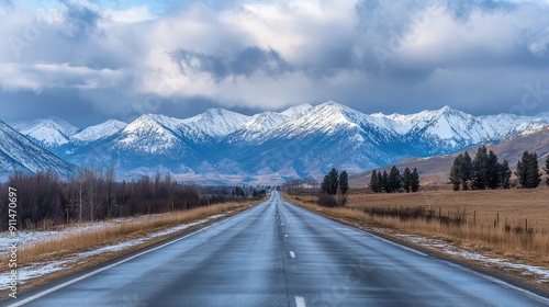 Highway disappearing into the distance with snow mountains and a cloudy sky, highlighting road trip landscapes.