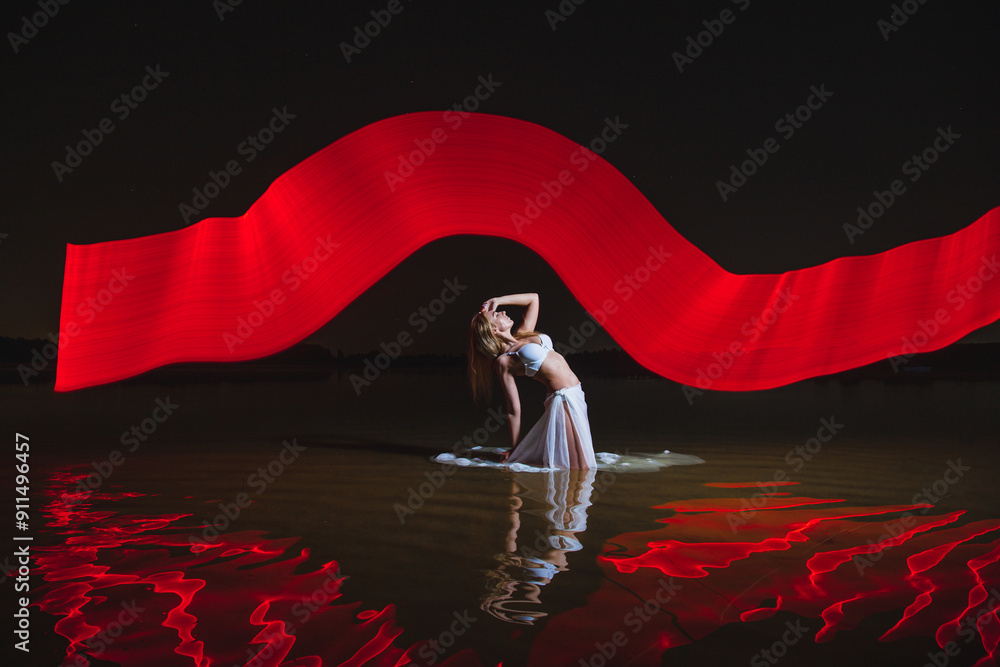 Young slim girl in white swimsuit posing in water at night with abstract red light effect