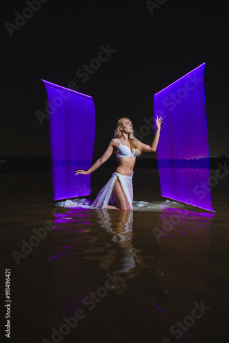 Obraz na płótnie Young slim girl in white swimsuit posing in water at night with abstract purple light effect w salonie